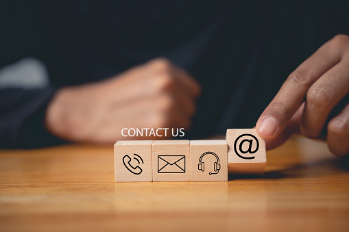 Contact us concept on website page. Customer support hotline and people connection. Wood cube with email, phone, address, and headset icons. Business communication banner.