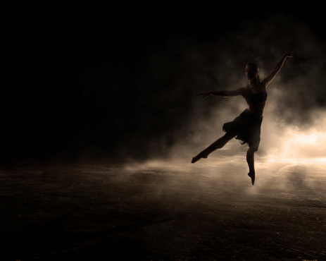Female dances by herself in the dark of the stage with fog and backlighting.