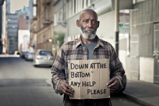 A homeless man holds a cardboard sign asking for help on the street.