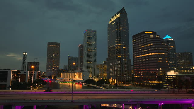 Highway traffic in Tampa city in Florida with brightly illuminated high skyscraper buildings in downtown district. American megapolis with business financial district at sunset