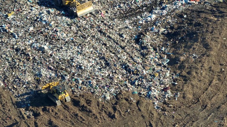 Garbage landfill site with bulldozer tractors burying large amount of trash under the ground. Harmful impact of open waste managment on environment