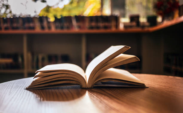 istock Vintage style.An open book or textbook vintage style in the library with light from the window on the reading table and the corridor of the bookshelves in the school classroom background.Education learning concept 1673186627