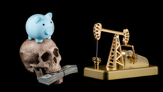 Golden oil pump, human skull, stack of 100 US dollar bills and piggy bank on black background