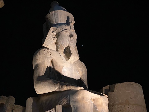 The ancient sitting statue of Ramses II in Luxor Temple lit up at night