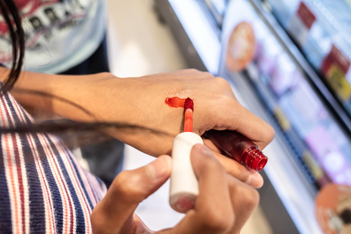 Teen girl smearing red color lipstick on the back of her hand at a beauty store
