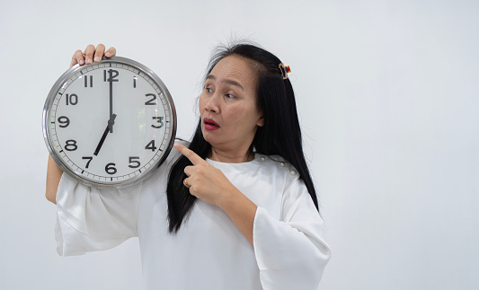 Studio shot of beautiful surprised Asian woman with clock while standing in front of white background. Concept of time management