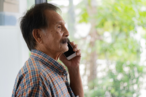 Side view portrait of elderly Asian male senior grandfather have call with relatives and use smartphone internet. Technology for older concept. copy space