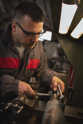 Young man is using measuring device in a metalworking shop, wearing protective workwear