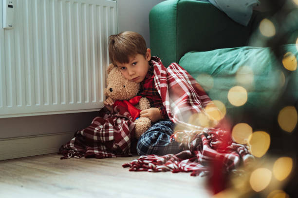 istock cute little boy wrapped id plaid sitting by heater 1673312645