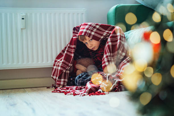 istock cute little boy wrapped id plaid sitting by heater 1673313168