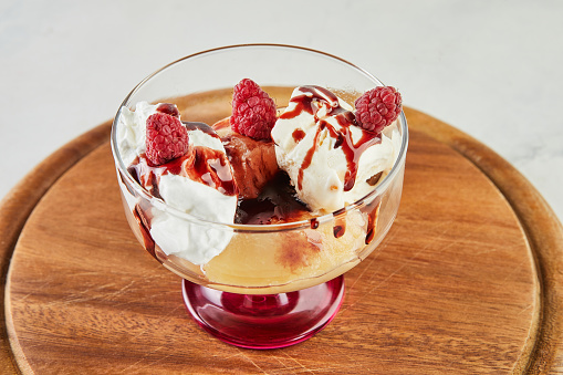 Dessert with raspberries, creamy ice cream and whipped cream in special glass.