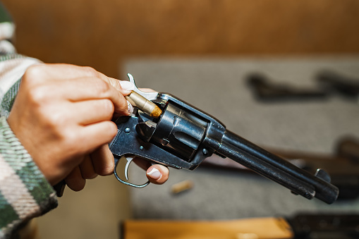 A girl loads an old cowboy revolver with cartridges, only the girl hands are in the frame. High quality photo