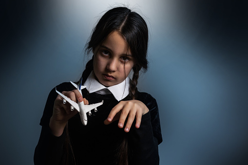 A girl with braids in a gothic style on a dark background with toy airplane.