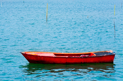 A small, white rowing boat is moored in a calm sea. The sun reflects gently on the water. The oars lie in the boat, ready for the next trip out.