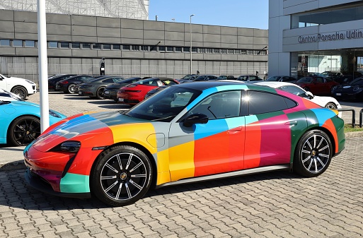 Udine, Italy. September 9, 2023. Multicolored Porsche Taycan Turbo outside the official dealer. It is a battery electric car of the luxury german automaker.