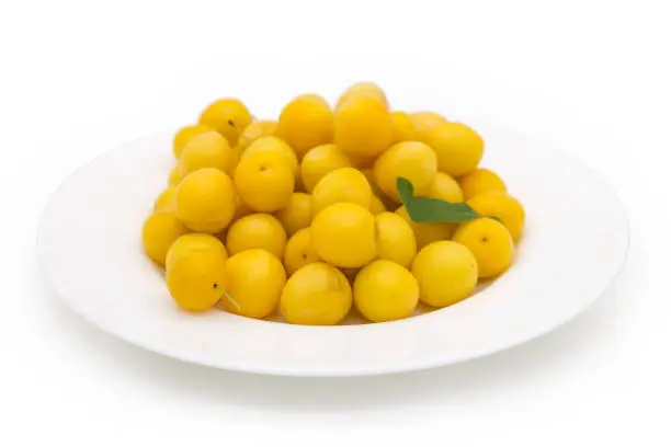 Freshly harvested yellow cherry plums on a white dish on a white background, side view in selective focus
