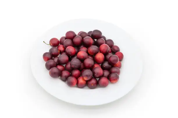 Ripe red cherry plums on a white dish on a white background