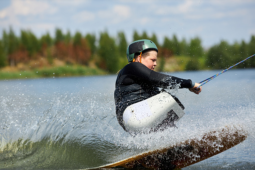 Action portrait of teenager with disability enjoying fast speed wakeboarding on water with adaptive equipment, copy space