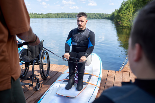 Full length portrait of adult man with disability in wakeboarding lesson using adaptive equipment, copy space