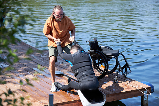 Portrait of senior sports instructor assisting man with disability using adaptive equipment for wakeboarding