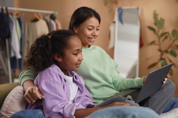 Black mother and daughter using laptop in room