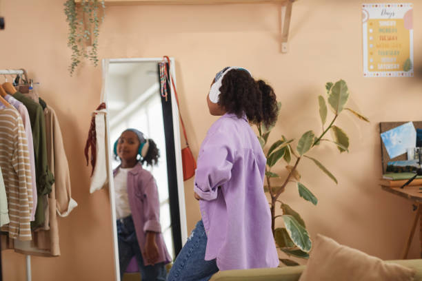 Back view of black girl dancing by mirror wearing headphones at home