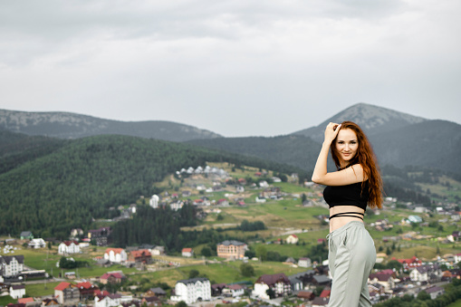 A beautiful young girl smiles against the background of the mountains in the summer. A village in the middle of the mountains. Beautiful landscape of mountains. The concept of tourism and travel.
