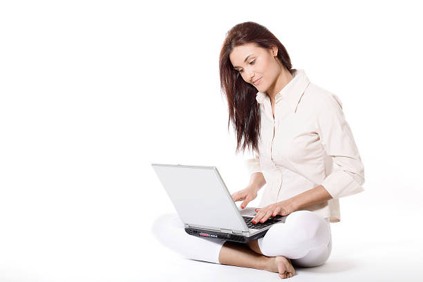 Woman in white clothes with laptop seated with crossed legs stock photo
