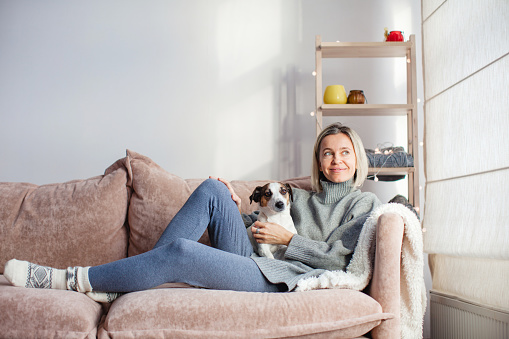 Contented, peaceful middle-aged woman is resting on the couch at home. Attractive adult lady spends the weekend with her dog