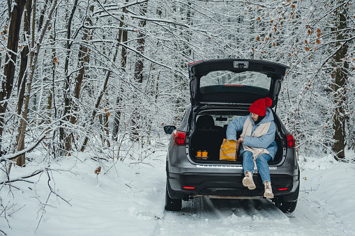 stop for lunch break. woman sits in trunk of her car and takes out food from package.