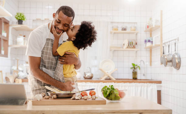 portrait of little american african black boy parent cooking preparing food with pan in the counter kitchen. happy  family with father son, father's day, healthcare cooking plant based food concept - family american culture african culture black imagens e fotografias de stock
