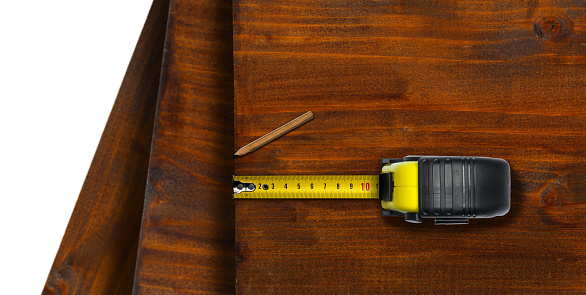 Close-up of a yellow and black tape measure and a pencil on wooden boards, isolated on white background with copy space.