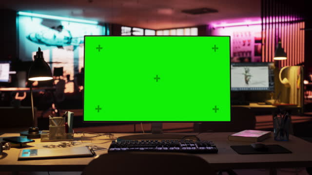 Desktop Computer with Mock Up Green Screen Chroma Key Display Standing on the Desk in the Empty Creative Office Lit by Neon Lights. Monitor in Game Development or Animation Company. Zoom Out