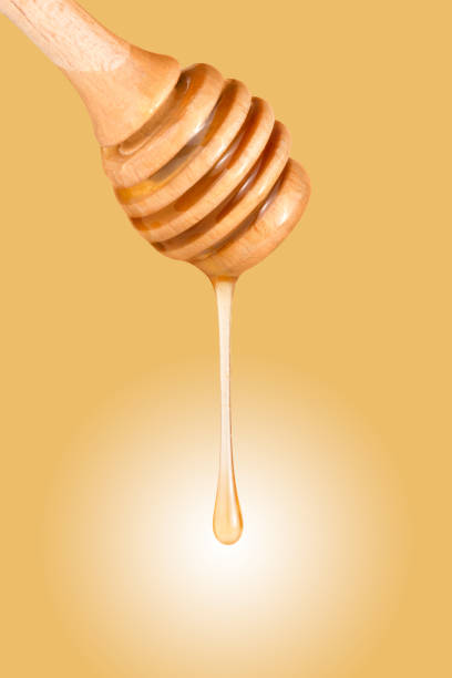 istock Honey flows down a wooden stick on a yellow background. 1673499390