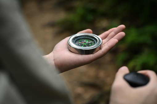 Closeup view of male hiker using compass for directions while exploring nature in the forest.
