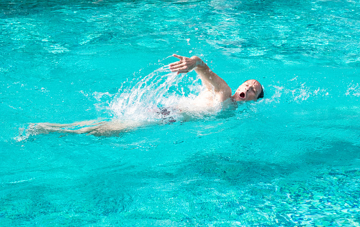 Mature active man swimming freestyle in outdoor swimming pool under the sun. Healthy lifestyle and sport concept