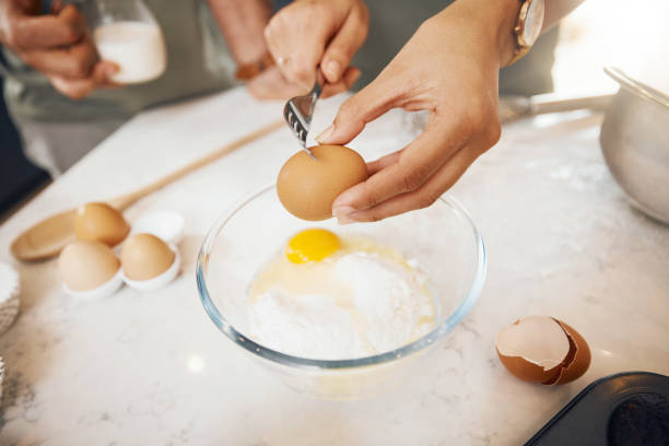 istock Hands with fork, crack egg and cooking in kitchen on bowl on table in home. Food, bakery and break eggshell for ingredient in flour for healthy diet, protein nutrition or person in pastry preparation 1673536552