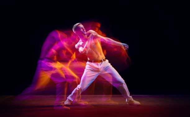 istock Inspiration and freedom. Young shirtless guy making chaotic movements against black studio background in neon with mixed lights effect 1673540893
