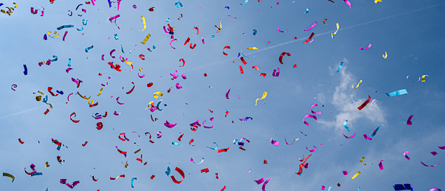 Colourful paper ribbons confetti falling against blue sky.
