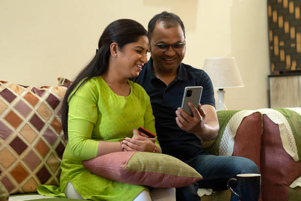 istock Husband wife sitting on sofa using smartphone 1673550209