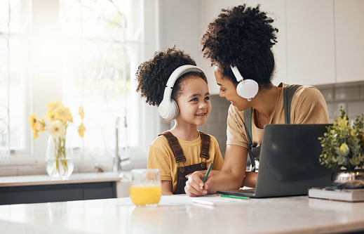 Online education, mother and child in home with headphones, laptop and homework for virtual class. Computer, mom and boy working together for elearning, help on writing and kid in kitchen with smile.
