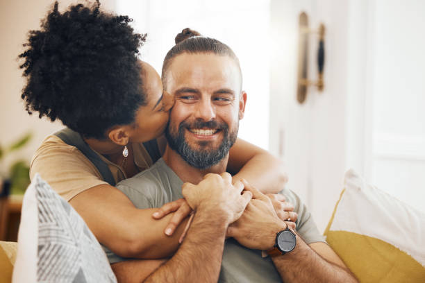 istock Interracial couple, hug and kiss, happy on couch and relax at home with bonding, commitment and affection. Healthy relationship, marriage and love with care and trust, people in lounge with romance 1673586375