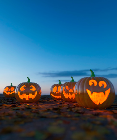 Selection of carved Halloween pumpkins on a leaf strewn ground at sunset glowing 3d render