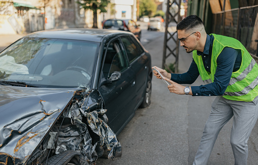 A seasoned insurance inspector with expertise examines the dented car bodywork of a damaged vehicle. His serious and focused demeanor underscores his dedication to thoroughly assessing the damage for insurance purposes