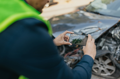 An insurance agent, a man in his early 30s, offers valuable support to the car owner during a challenging time. With a mobile phone in hand, he meticulously documents the damaged car, ensuring a smooth car insurance claim process amidst the misfortune.