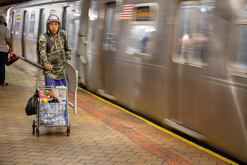 21th Street Queensbridge Subway Station, Long Island City, Queens, New York, USA - August 23th 2023:  Man walking down the platform with a trolly and a table in front of a arriving subway train