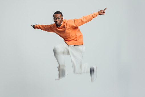 Full shot studio portrait of a young male model jumping in the air with his arms outstretched. His legs are blurred because of the movement.