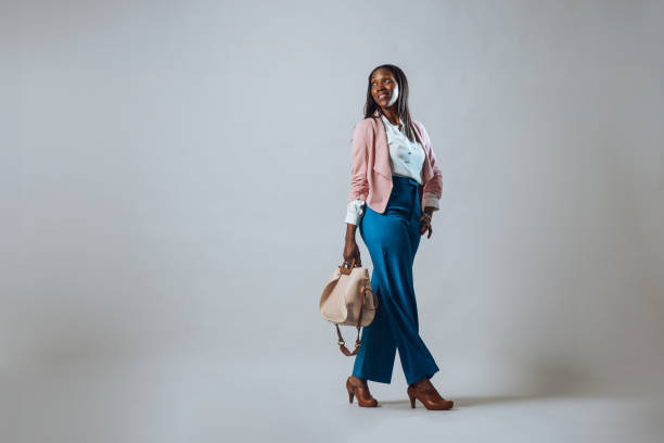 Embracing the Good Vibes Full studio portrait of a mid-adult female walking looking away from the camera. She is wearing a pink cardigan and blue trousers, holding a handbag. older woman purse stock pictures, royalty-free photos & images