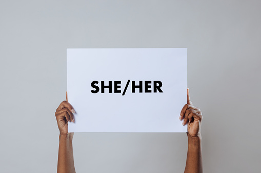 A cropped shot of an unrecognisable person's arms holding a white sign displaying the words she and her on it.