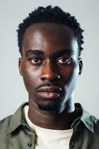 Close-up studio portrait of a young male model looking into the camera with a serious expression. He is wearing a T-shirt and an overshirt.